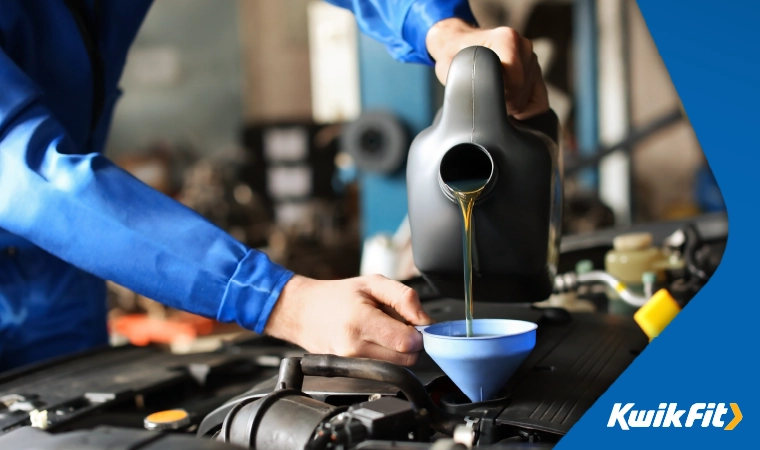 Technician in blue boiler suit pouring oil into a funnel.