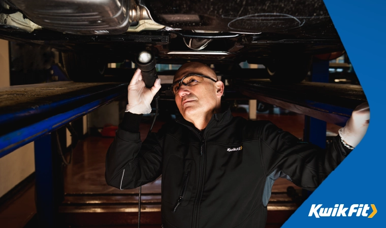 Kwik Fit technician wearing safety glasses inspecting the underneath of a car.