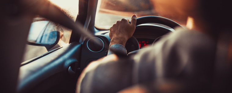 Person driving a car into a sunset